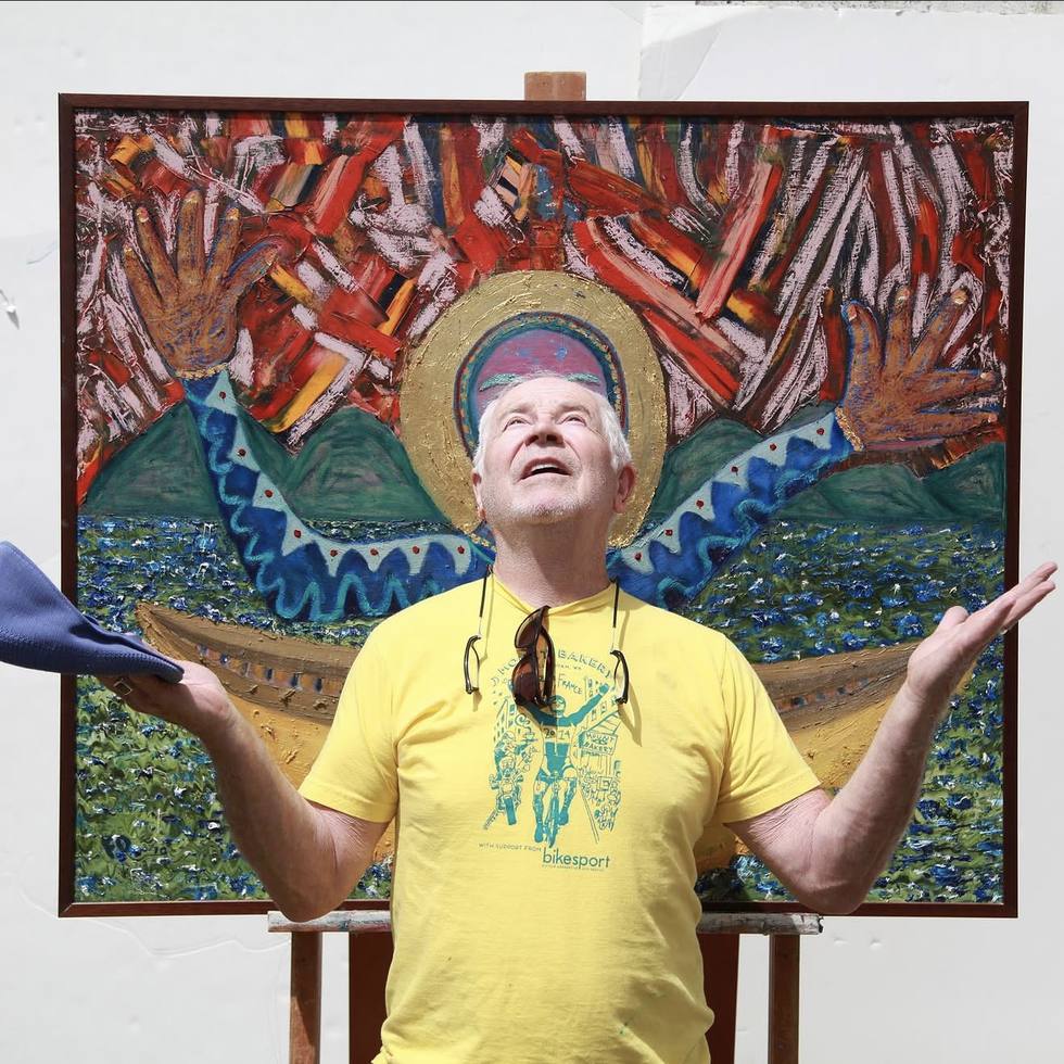 Frank standing in front of his painting Seek Grace with his arms open, looking upward