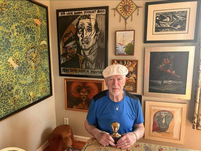 Frank holding a small gold trophy in his studio, surrounded by framed work